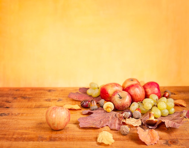 mesa de madeira com maçãs, uvas e folhas de outono em um fundo amarelo com espaço de cópia