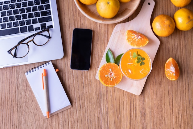 Mesa de madeira com mesa de escritório com copo de suco de laranja e smartphone de tela em branco.