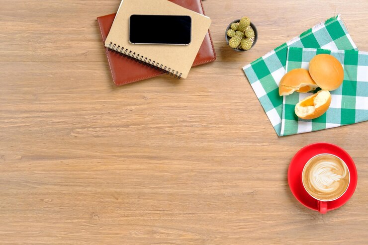 Foto mesa de madeira com notebooks, telemóvel, padaria e xícara de café com espaço para cópias