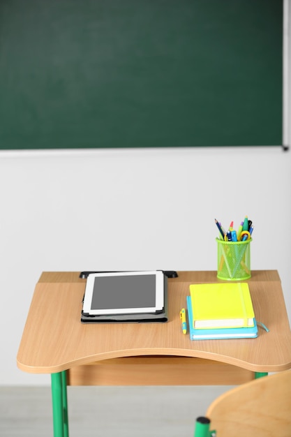 Foto mesa de madeira com papelaria e tablet em aula no fundo do quadro-negro
