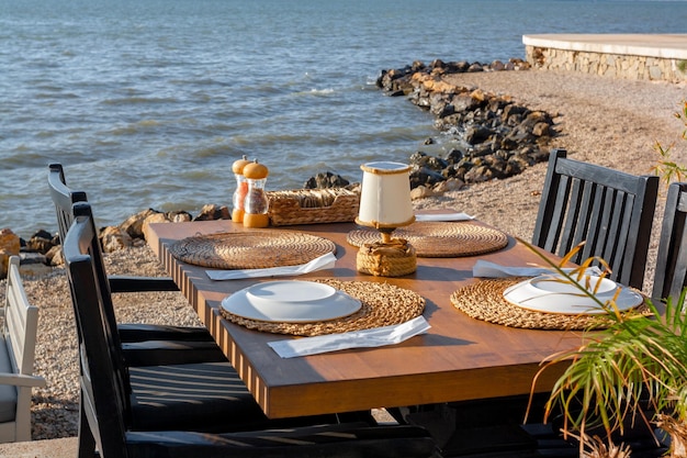 Mesa de madeira e cadeiras com pratos no café à beira-mar estão esperando por convidados