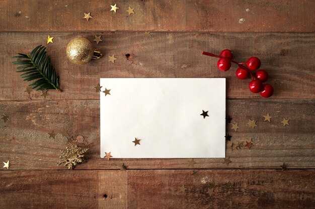 Mesa de madeira plana com envelope branco e enfeites de natal ao redor