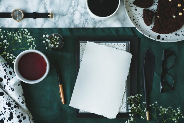 Mesa de mármore com pano verde na foto de vista superior com óculos xícara de chá relógio papel em branco e caneta de pena