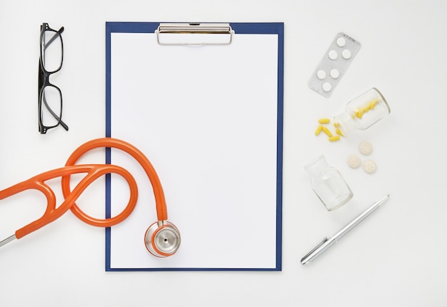 Mesa de médico com medicamentos, estetoscópio e óculos, vista superior