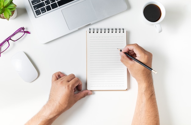 Mesa de mesa de escritório branco com homem mão escrevendo no caderno em branco