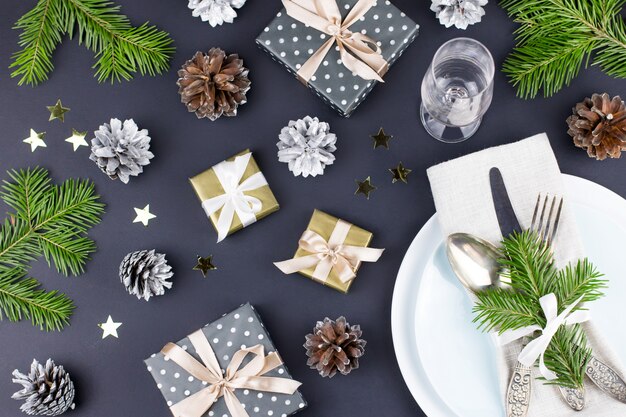 Mesa de Natal com pratos, talheres, caixa para presente e enfeites nas cores preta e dourada. Vista do topo