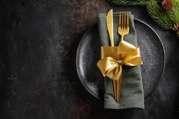 Mesa de Natal servida em tons escuros com decoração dourada.