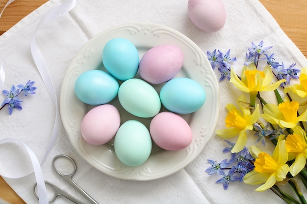 Mesa de Páscoa com ovos coloridos em um prato e um buquê de narcisos