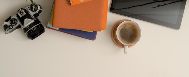 Mesa de trabalho branca com espaço de cópia, câmera, cadernos, tablet digital e xícara de café