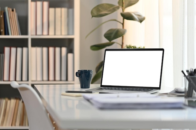 Mesa de trabalho branca no escritório doméstico moderno com xícara de café de computador portátil e documentos Tela em branco para design de publicidade