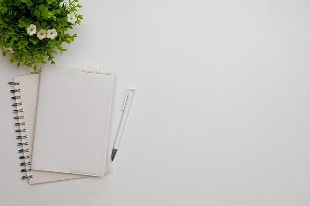 Mesa de trabalho branca simples com planta de decoração de caneta de caderno espiral e espaço para cópia