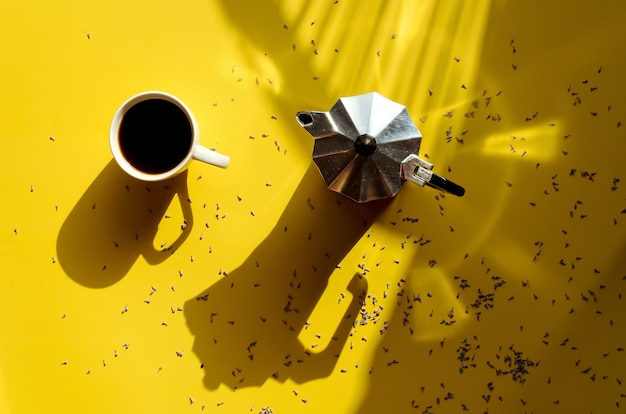 Mesa de trabalho com cafeteira francesa e xícara de café quente em fundo amarelo. Vista superior