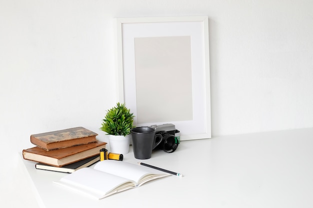 Mesa de trabalho com câmera de fotografia, livro, bloco de notas e lápis na mesa branca