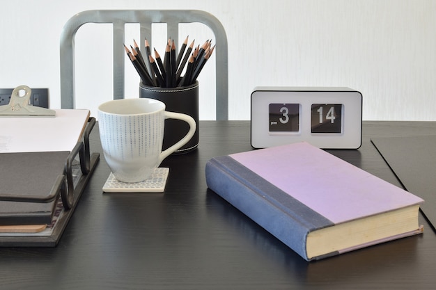 Foto mesa de trabalho com livro, lápis, xícara de café e relógio em uma casa