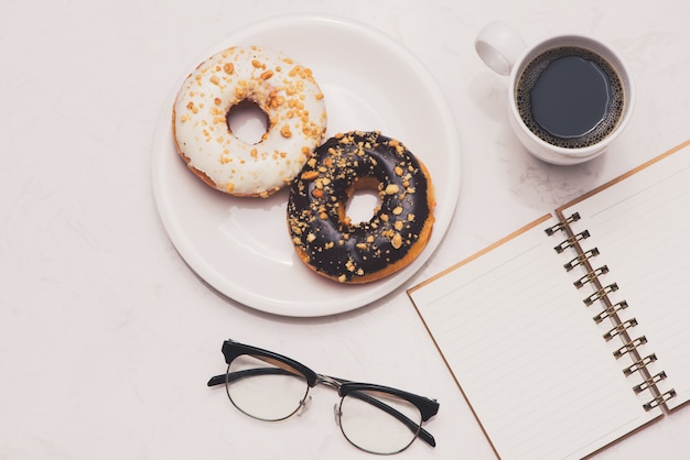 Mesa de trabalho com sobremesa e café. Bolo donuts com uma xícara de café expresso no tampo da mesa de mármore.