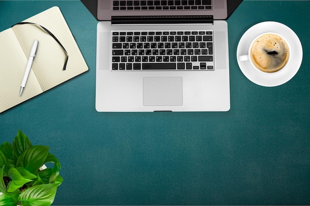 Mesa de trabalho com uma xícara de café e laptop, caderno, caneta