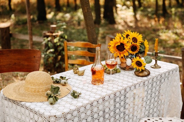 Mesa decorada con mantel de crochet, botella de vino, girasoles y sombrero de paja