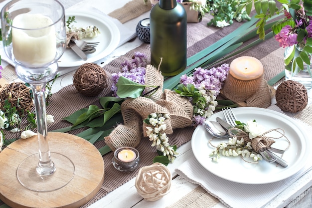 Mesa decorada maravillosamente elegante para vacaciones con flores de primavera y verdes - boda o día de San Valentín con cubiertos modernos, arco, vidrio, velas y regalos, horizontal, primer plano, tonificado