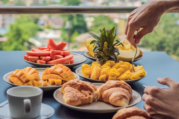 Mesa de desayuno con café, fruta y croissant de pan en un balcón con el telón de fondo de la gran ciudad