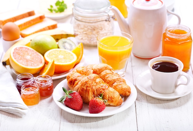 Mesa de desayuno con croissants, café, jugo de naranja, tostadas y frutas.