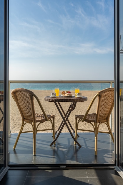 Mesa con desayuno y dos sillas en el balcón de un hotel junto a la playa