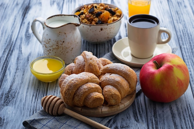 Mesa de desayuno con granola, croissants, manzana, café, zumo.