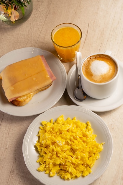 Mesa de desayuno con huevos, taza de café, jugo de naranja y rebanada de pan con queso y tocino.