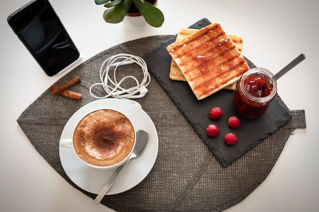 Mesa de desayuno con mermelada y pan y café capuchino caliente - lugar de trabajo desde casa