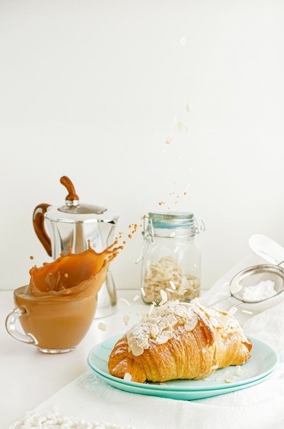 Mesa de desayuno. Salpicaduras de café y caída de hojuelas de almendras en croissant. Concepto de comida voladora. Copia espacio