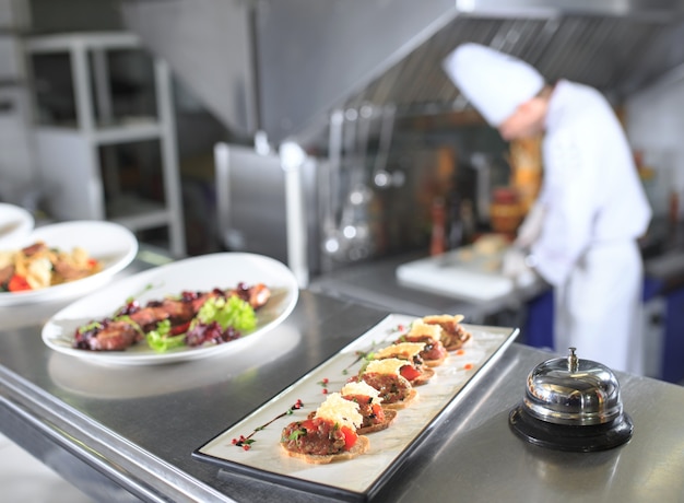 La mesa de distribución en la cocina del restaurante. El chef prepara una comida en el fondo de los platos terminados.