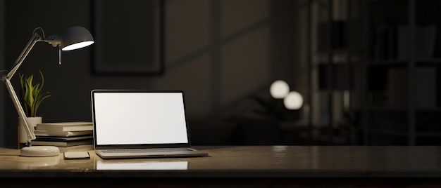 Mesa do espaço de trabalho com luz de maquete de laptop do candeeiro de mesa sobre a sala de escuridão turva