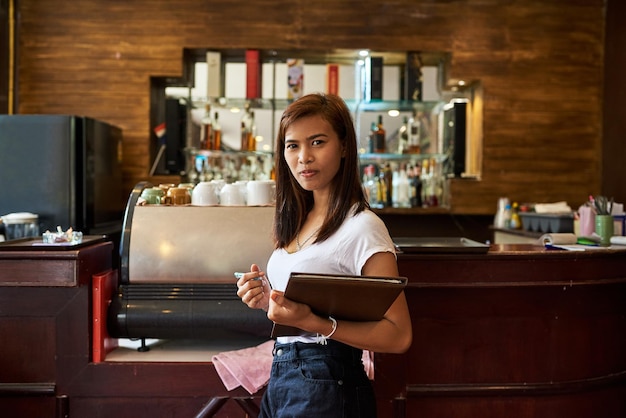 Foto mesa para dos retrato de una amable camarera esperando para servir a los clientes en un restaurante tailandés.