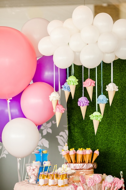 mesa con dulces y postres, nubes de globos y helados y muchos globos de colores y grandes juguetes de caramelo