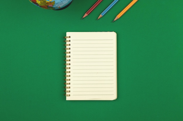 Mesa escolar verde com caderno pautado em branco e foto com vista superior a lápis com espaço de cópia