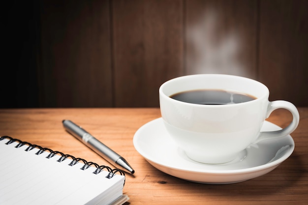 Mesa de escritorio de madera con café. Espacio de trabajo con cuaderno, bolígrafo y taza de café en el espacio de madera con espacio de copia.