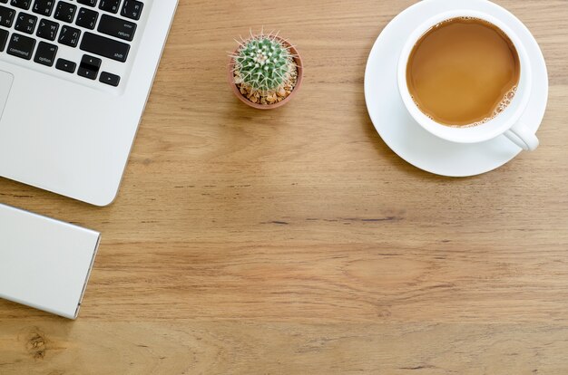 Mesa de escritorio de madera con computadora portátil, disco duro externo, cactus y taza de café. Vista superior con espacio de copia.