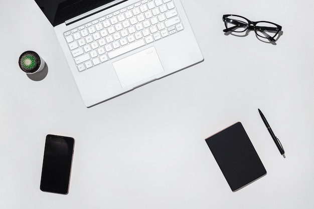 Mesa de escritorio moderna para estudiantes con computadora portátil, teléfono inteligente con pantalla en blanco, lentes con estilo, cuaderno negro y bolígrafo