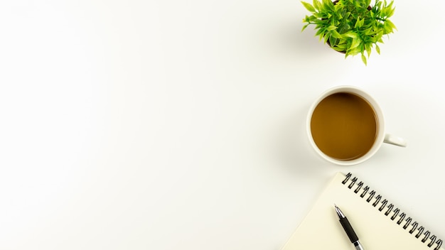 Mesa de escritorio de oficina blanca con taza de café y una pluma en el cuaderno en blanco