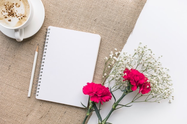 Mesa de escritorio de oficina en casa con bloc de notas, ramo de flores sobre fondo de tela de saco.