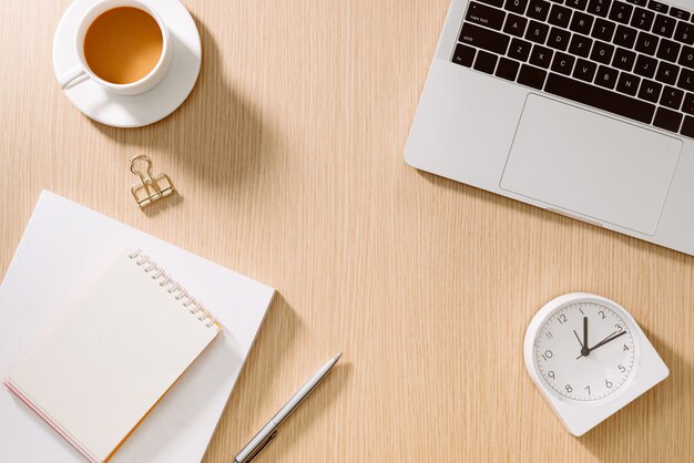 Mesa de escritorio de oficina con computadora portátil, teléfono inteligente, taza de café, bolígrafo, lápiz y cuaderno. Suministros de oficina y gadgets en la mesa de escritorio. Concepto de mesa de escritorio de trabajo.