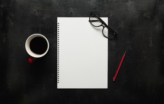 Mesa de escritorio de oficina de madera negra con anteojos, cuaderno y bolígrafo con taza de café