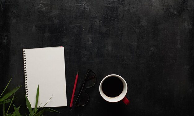 Mesa de escritorio de oficina de madera negra con anteojos, cuaderno y bolígrafo con taza de café