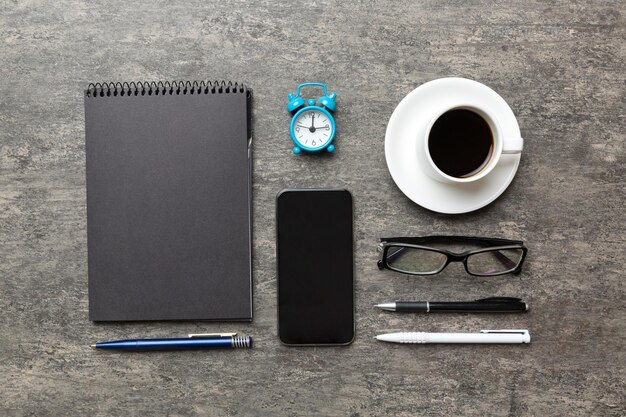 Mesa de escritorio de oficina moderna con teléfono inteligente portátil y otros suministros con taza de café Página de cuaderno en blanco para su diseño Vista superior plana