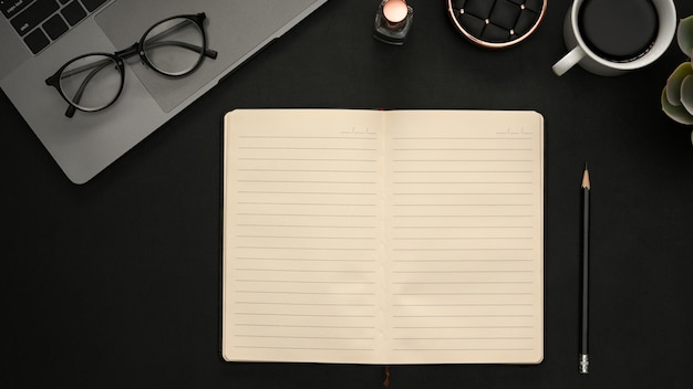 Mesa de escritorio de oficina negra moderna con páginas de cuaderno en blanco para ingresar el texto y los suministros de oficina