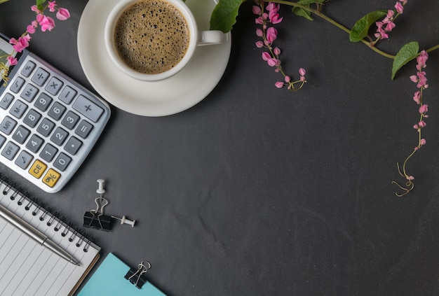 Mesa de escritorio de piedra negra de la oficina con la calculadora, café sólo y pluma y enredadera de flor rosa, busine