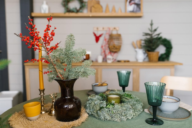 Mesa festiva en la cocina para Navidad y Año Nuevo Ramas de abeto en un jarrón vasos de vidrio una vela una corona en la mesa