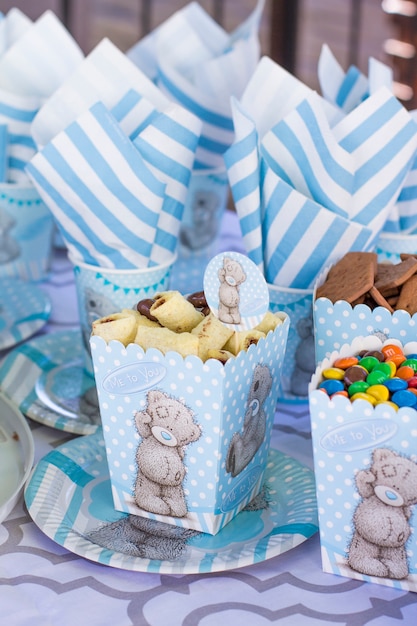 Mesa festiva para niños. Decoración para fiesta infantil. Oso de peluche estilo servir. Paquetes, galletas, tazas, platos y servilletas son de color blanco azulado.