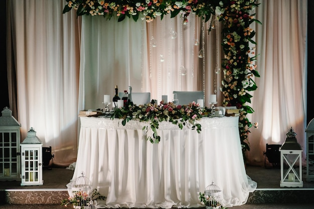 Mesa festiva para recién casados cubiertos con un mantel y decorados con una composición de flores y velas verdes en el salón de banquetes de bodas Fiesta de bodas en carpa