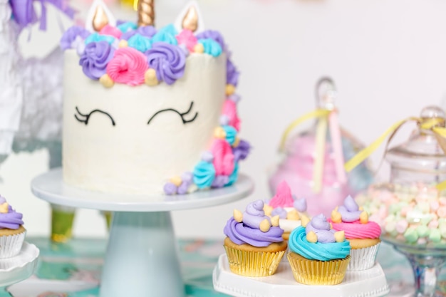 Mesa de fiesta de cumpleaños de niña pequeña con pastel de unicornio, cupcakes y galletas de azúcar.