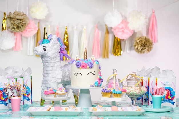 Mesa de fiesta de cumpleaños de niña pequeña con pastel de unicornio, cupcakes y galletas de azúcar.